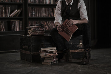 pensive man stands at night in a dark library room and holding a vintage book. stylish man with a mustache straightens the bracelet.