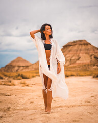 Fototapeta na wymiar A young brunette Caucasian girl in a white dress and a black bikini walking barefoot through a desert