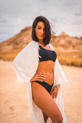 A young brunette Caucasian girl in a white dress and a black bikini posing in the desert of Las Bardenas