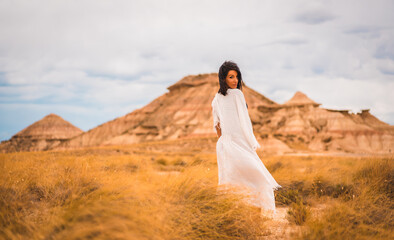 Fototapeta premium Young brunette Caucasian girl in a white dress and a black bikini enjoying in the beautiful desert