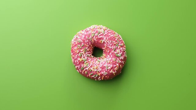 Fresh sweet doughnut covered by frosted pink chocolate bright sprinkle rotating isolated on green
