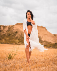 Fototapeta na wymiar Portrait of a young brunette Caucasian model wearing a white dress and a black bikini in the beautiful desert one summer afternoon, vertical photo