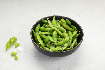 Raw edamame soya beans with salt and sauce on light gray background.