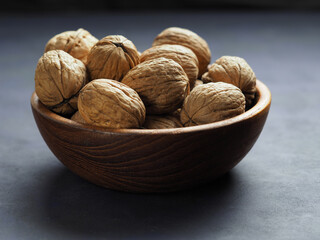 Walnuts in a wooden bowl on a dark background.