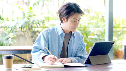 Online studying class, Student man hand writing on notebook while using digital tablet for e learning, Adult male university, college student study online course at home, education, Work from home