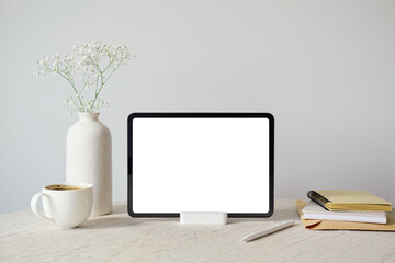 Blank screen tablet mockup, vase of gypsophila flowers, cup of coffee, notebooks on table with...