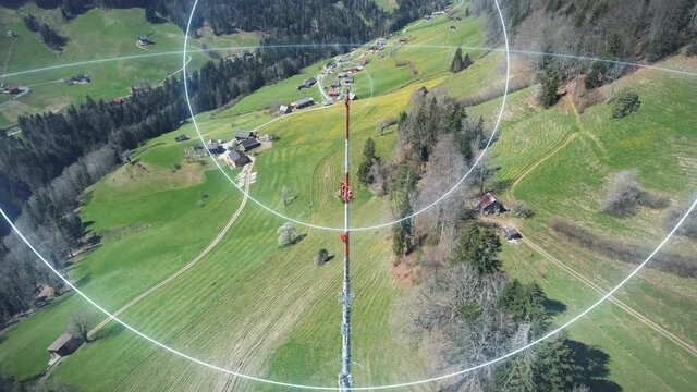Telecommunication mast on mountain surrounded by green meadows sends 5G network data streams in all directions