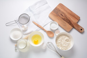 Frame of food ingredients for baking on a white background. Flour, eggs, sugar and milk in white and wooden bowls . Cooking and baking concept.