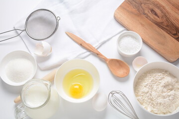 Obraz na płótnie Canvas Frame of food ingredients for baking on a white background. Flour, eggs, sugar and milk in white and wooden bowls . Cooking and baking concept.