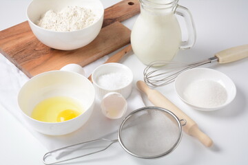 Fototapeta na wymiar Frame of food ingredients for baking on a white background. Flour, eggs, sugar and milk in white and wooden bowls . Cooking and baking concept.
