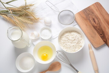 Frame of food ingredients for baking on a white background. Flour, eggs, sugar and milk in white and wooden bowls . Cooking and baking concept.