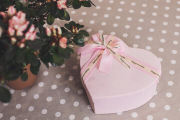 Cute gift with love for mom. Surprise. Pink heart-shaped box and beautiful flowerpot on the dotted tablecloth 