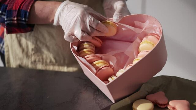 Woman in gloves puts macaroni in gift box from tray