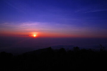 Landscape Tranquil scene of the sunrise with Orange sky and fog around the mountain in the morning at doi pha hom pok national park Thailand.