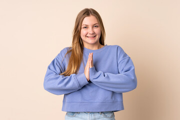 Teenager Ukrainian girl isolated on beige background keeps palm together. Person asks for something