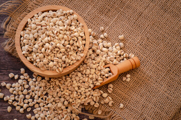 Bowl of Adlay millet or pearl millet or Job's tears in wooden bowl on the sackcloth over wooden table background. copy space for text. Healthy food.