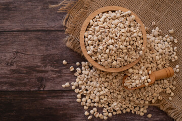Bowl of Adlay millet or pearl millet or Job's tears in wooden bowl and wooden scoop on the sackcloth over wooden table background. copy space for text. Healthy food.