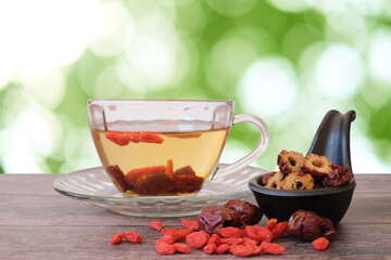 Healthy hot drink brewed from Chinese jujube and Chinese goji berries in glass and sliced Chinese date in the black cup on wooden background with  green blurred garden background. 