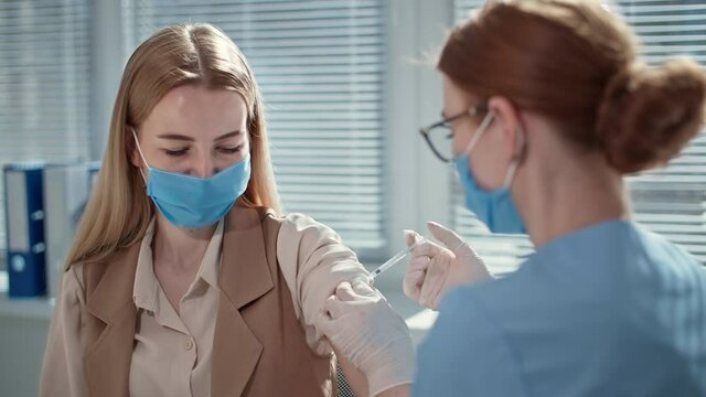 nurse wearing protective gloves uses syringe to inject virus vaccine to treat female patient