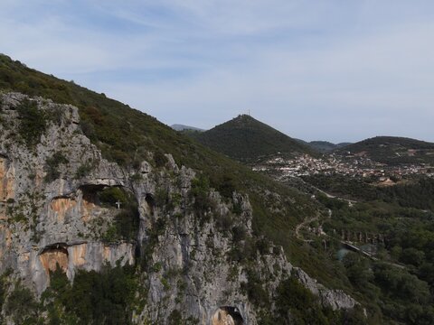 Aerial drone view dragon hole of St. George in the mountain ridge next to the river louros and the roman aqueduct of ancient nikopolis in preveza, epirus, greece.