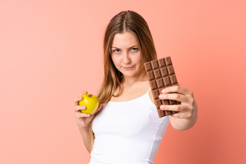 Teenager Ukrainian girl isolated on pink background taking a chocolate tablet in one hand and an apple in the other