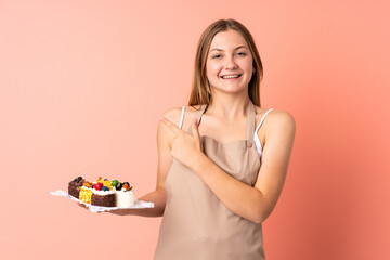 Pastry Ukrainian chef holding a muffins isolated on pink background pointing finger to the side