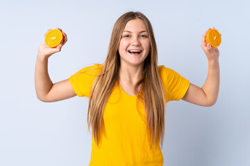 Teenager Ukrainian girl isolated on blue background holding an orange