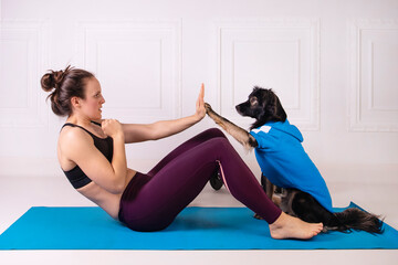 Sport with a dog. Attractive girl working out on the blue fitness mat with her dog. Athletic woman doing exercise. Strength and motivation, sport and healthy lifestyle. Female fitness.