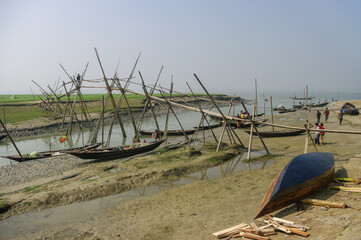 Rural landscape view of traditional bamboo bridge above sea water channel and wooden fishing boats with bay of Bengal in the background, Mehendiganj, Barisal, Bangladesh