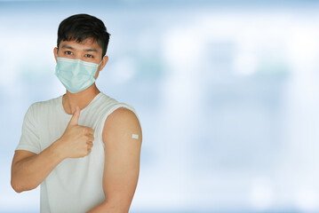 close up young asian man with protective face mask sand showing bandage on shoulder to expression after got corornavirus antibody vaccinated isolated on blur hospital background for health concept