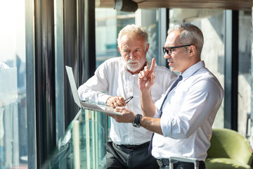 Two business man discussing their idea on their laptop in a hotel lobby. They are sharing idea and the younger man is pointing his finger upwards