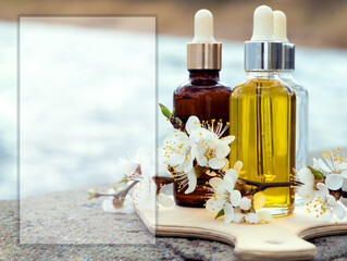 Glass bottles with cosmetic serum of different colors, apricot flowers stand on a concrete parapet against the background of glittering water. Selective focus, advertising layout, outside.