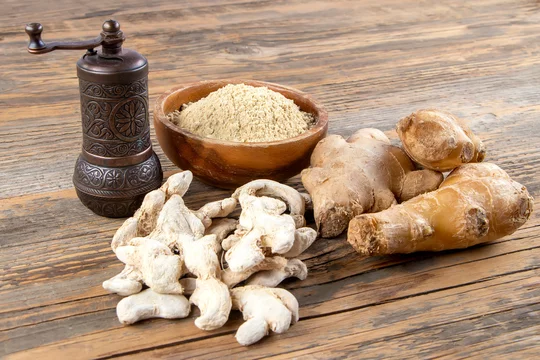 Fresh ginger root, dried ginger and ground ginger powder in wooden bowl on  wooden rustic table near old grinder. Healthy food spice concept. Zingiber  officinale. Stock Photo
