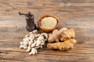 Fresh ginger root, dried ginger and ground ginger powder in wooden bowl on wooden rustic table near old grinder. Healthy food spice concept. Zingiber officinale.