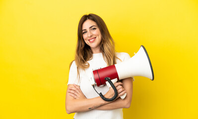 Caucasian woman isolated on yellow background holding a megaphone and smiling