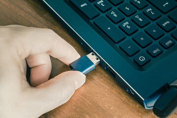 Male Hand Connecting A Black USB Cable To The USB Port Of A Black Notebook