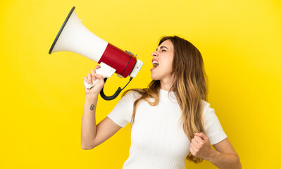 Caucasian woman isolated on yellow background shouting through a megaphone to announce something in lateral position