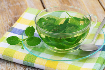 Fresh mint tea in transparent glass on checkered cloth on rustic wood
