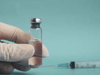 Doctor's Hand in white gloves hold the vial with vaccine or drug on blue background. Vaccination concept. Development of the COVID-19 coronavirus vaccine. Space for text