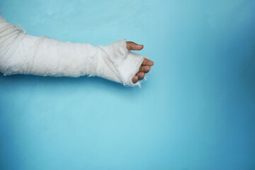 injured painful hand with bandage against blue background 