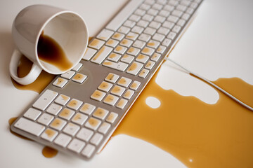 Spilled black coffee on a computer keyboard at a white table