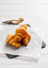 Board with tasty croissants on dark wooden table, closeup.