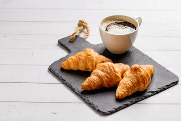 Coffee white cup, croissants on white wooden table background, selective focus. Breakfast concept