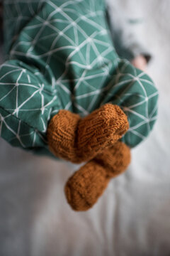 Neugeborenes Baby mit gr&uuml;nem Strampler und orangen Wollsocken oder Wolls&ouml;ckchen liegt auf wei&szlig;em Mulltuch