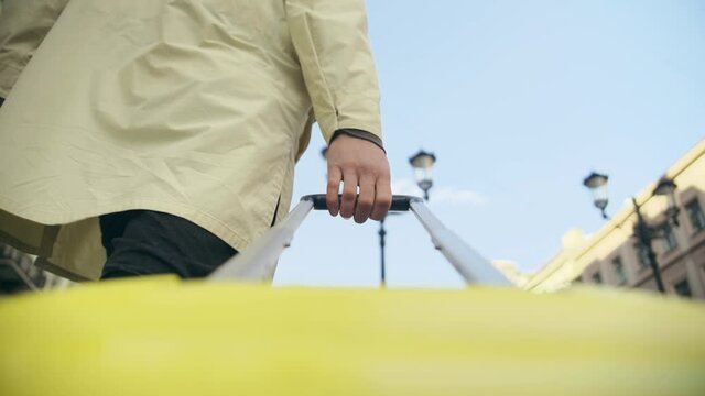 Slow motion camera is rigged on a yellow travel suitcase with a long handle. A man's hand pulls a large bag along the street. a traveler in a yellow raincoat walks down the street.