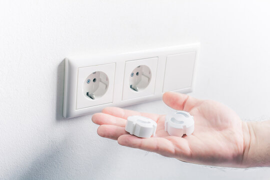Hand Holding Baby Safety Plugs In Front Of A Wall Socket - Child Safety Concept