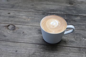 A cup of coffee with late art pattern in a white cup on wooden background with copy space.