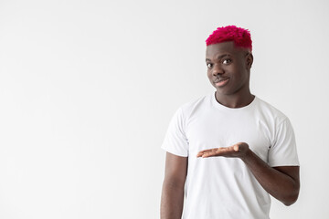 Naklejka premium Satisfied black man. Advertising product. Promotion action. Good offer. Big sale. Smiling african guy with bright pink hair white t-shirt showing copy space open palm isolated light.
