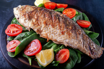 Grilled fish with tomatoes, spinach on a wooden board. Delicious and light dinner