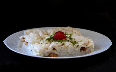 Ramadan dessert Güllaç on the plate. It is made with Güllaç, milk, rose water, walnut, vanilla and phyllo dough. It is decorated with cherries and pistachios.
